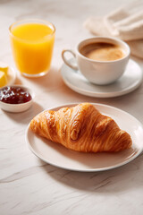 Photo shoot of a continental breakfast croissant, jam, butter, orange juice and coffee on a light marble table.