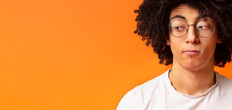 Black millennial man with expression of suspicion his face, looking skeptically aside at empty space, orange panorama background