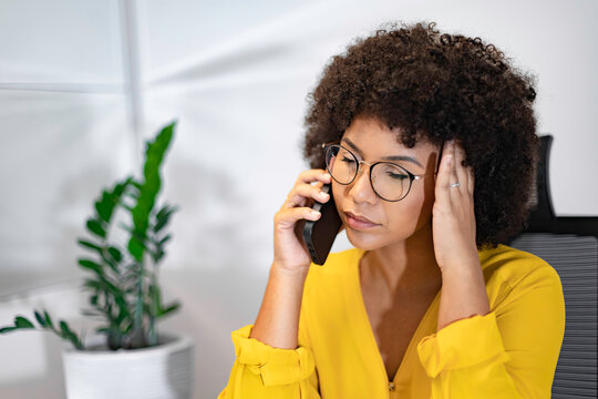 Young Black woman in yellow shirt feeling stressed during a phone call in home office. Concept of customer service, work pressure, frustration, or business conflict.
