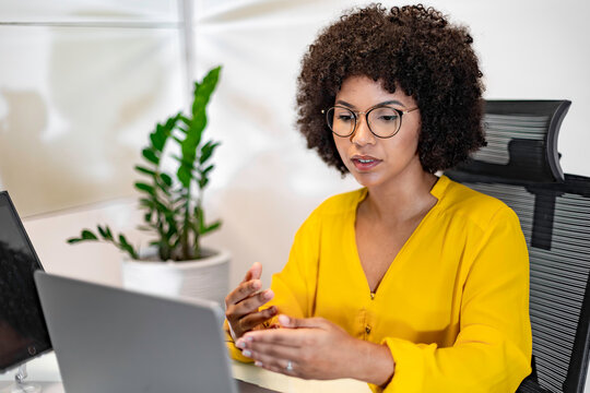 Focused Black woman talking during a video call or virtual meeting at her desk in a modern office. Confident communication in a professional and inclusive environment.