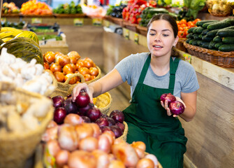 Young woman in apron sells onions in vegetables shop