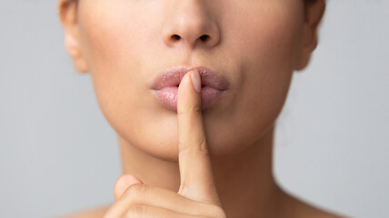 Fototapeta premium Women's secret. Woman holding finger on lips over grey background