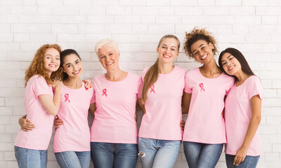 Happy Multiracial Ladies In Breast Cancer Pink T-Shirts With Awareness Ribbons Embracing Standing...