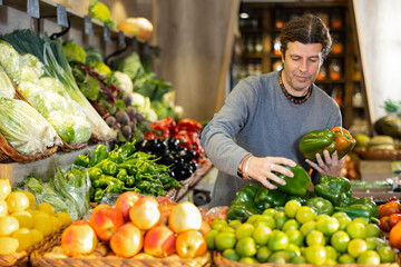 Adult man chooses bell pepper for purchase in vegetable shop