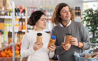 Couple choose for canned beans and lentils. European shoppers holding a jar of beans in his hands