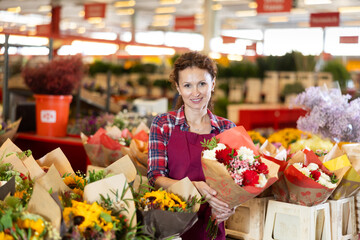 Female consultant seller holds bouquet of cut flowers in hands, gets acquainted with assortment,...