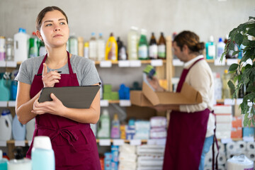 During inventory, stores female employee using tablet count and check number of detergent packages, write down data in questionnaire, enter data into invoice. Man employee in background