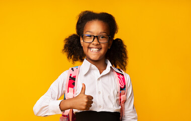 Cheerful Black School Girl Gesturing Thumbs-Up Smiling To Camera Posing Over Yellow Studio Background. I Like School Concept. Panorama