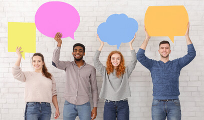 Happy students holding empty speech bubbles and looking at camera over white wall