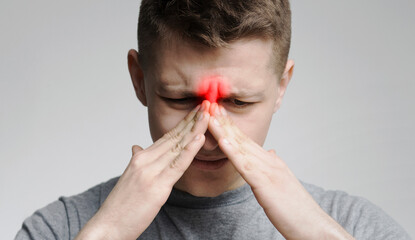 Chronic sinusitis. Young man touching his inflamed hose, close up