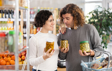 Spouses took varieties of pickled green olives jar from shelf, chooses olives. Customer read...