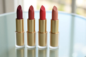Obraz premium Four different shades of red and nude lipstick in elegant gold tubes are arranged in a row, showcasing a collection of classic and modern beauty cosmetics