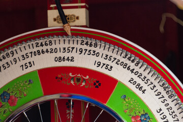 A red, blue and white colored wooden board with numbers in a circle. The spin wheel is for betting at a carnival. The fortune wheel spins in a circle and lands on a number that must match a ticket.