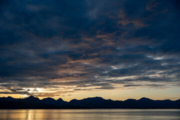 Dramatic Sunset/Sunrise Over Lake & Mountain Silhouettes: Golden Hour Reflections on Water with Moody Clouds – Nature's Tranquil Majesty