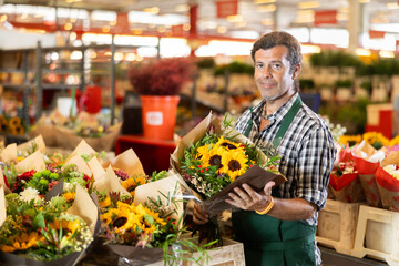 Male consultant seller holds bouquet of cut flowers in hands, gets acquainted with assortment, checks goods before sending them to customer.