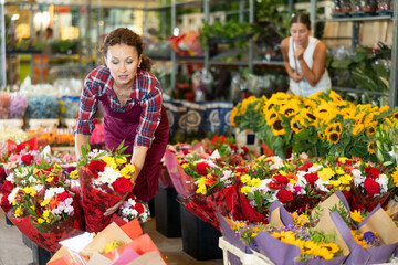 Adult female seller holding bouquet of flowers in flower shop