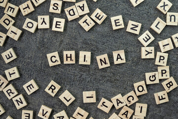 Wooden word block tiles spelling China are arranged on a top of black background table from a bird's eye view, highlighting the natural texture and warm lighting