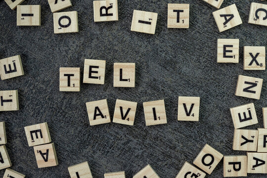 Wooden word block tiles spelling Tel Aviv are arranged on a top of black background table from a bird's eye view, highlighting the natural texture and warm lighting - Powered by Adobe