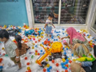 Obraz premium Abstract blurry and out of focus photo of children accompanied by their parents playing with plastic sand and toys in an indoor playground
