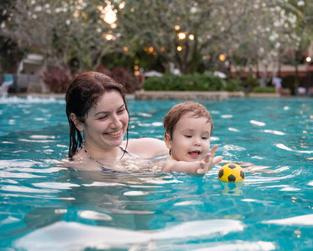 Caucasian woman holds her son while swimming in a pool on vacation. Mom teaches little boy to swim. 