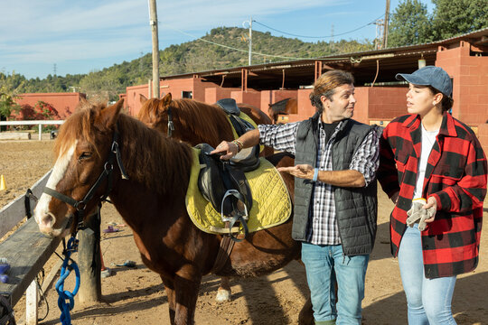 Owner of the stable offers young woman ride on a horse - Powered by Adobe
