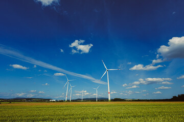 Wind Turbines Gracefully Positioned on Expansive Green Fields Under a Clear and Vibrant Blue Sky A...