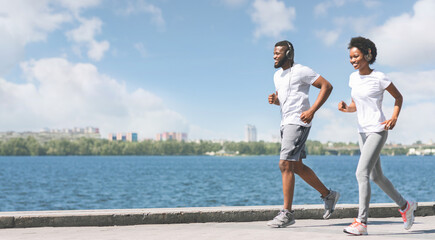 Morning Workout. Cheerful African American Couple Jogging Along River Embankment In City. Panorama,...