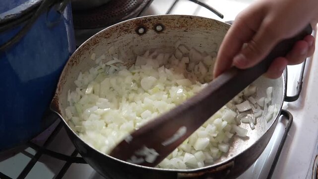Sauteing finely chopped white onions in a rustic pan