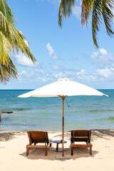 Tropical beach scene with two lounge chairs under white umbrella, overlooking a serene ocean and...