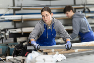Young woman worker in uniform taking steel profile pipe in warehouse