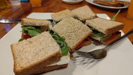 Plate of freshly made triangle sandwiches with mozzarella cheese, tomato, and basil on whole wheat bread. A healthy snack or light lunch served on a white plate in a cozy cafe setting.