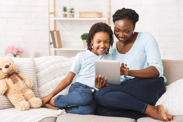 Online Shopping Concept. Cheerful black mom and daughter browsing internet using digital tablet,...