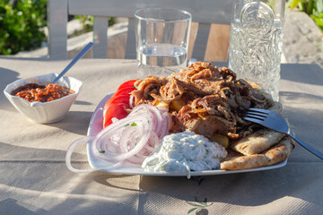 Fried pork pieces (gyros) with sauce, vegetables and French fries on the table close-up