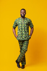 Handsome black man in traditional african green clothes posing over yellow studio background