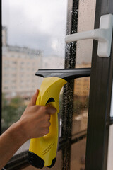 Close-up of male hand using cordless vacuum cleaner for cleaning window, wiping away water drops on rainy day, ensuring spotless and hygienic indoor environment. Concept of household cleanliness.