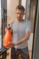Blurred vertical portrait of homeowner cleaning solution onto large window in high-rise building, preparing to wipe away dirt and grime for sparkling clean finish. Concept of hygiene and cleanliness.