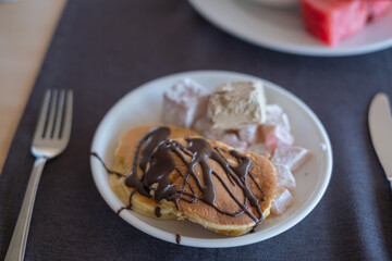 Delicious pancakes topped with chocolate sauce and accompanied by dessert cubes at a cozy breakfast table
