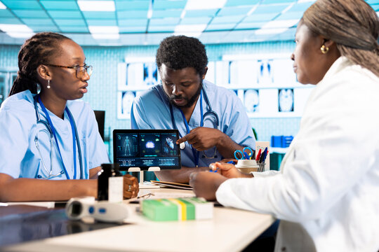 African american medic practitioner leading a young healthcare team in a cabinet, analyzing MRI imaging results and providing accurate diagnosis and effective treatment. Medical facility. - Powered by Adobe