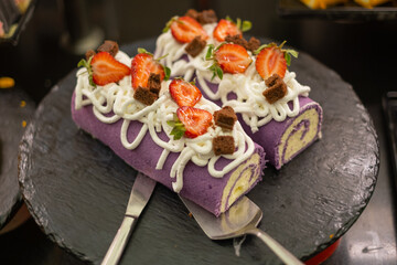 Delicious purple cake roll topped with strawberries and whipped cream at a dessert table in a bakery during a festive celebration