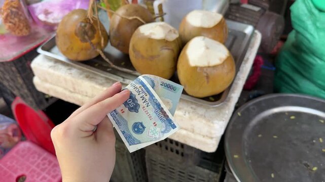 A tourist girl holds 25,000 Vietnamese dong in her hands and plans to buy a coconut at a local night market in Asia.