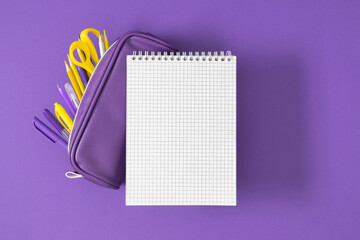 Top view of open notebook and purple pencil case with pencils and pens on purple background. Perfect for school theme. Back to school background.