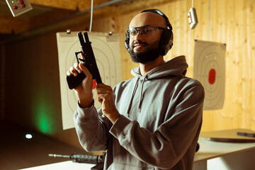 Smiling Arab shooting range client wearing protective glasses reloading gun following safety...