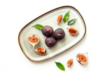 Purple ripe figs and slices with leaves on a plate top view on a white background