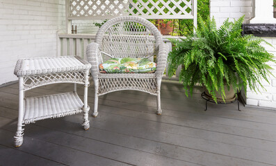 A white wicker chair with a potted fern on a white brick verandah
