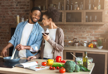Happy african-american couple cooking dinner together and drinking red wine