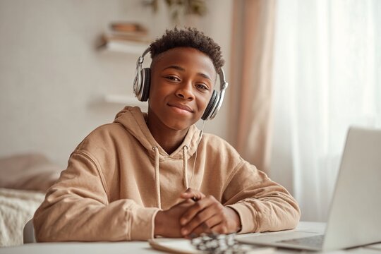 Young African American boy wearing headphones is sitting at a desk with a laptop, smiling confidently, showcasing a modern learning environment and engagement with technology - Powered by Adobe