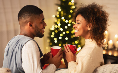 Excited black couple drinking coffee on Christmas eve, enjoying cozy evening at home