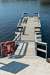 Wooden dock extending over calm water with a lifebuoy in a serene lakeside setting
