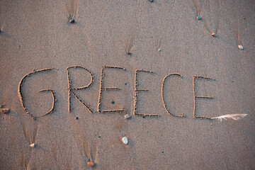 Word Greece written by hand on sand beach. The concept of tourism in this beautiful paradise country