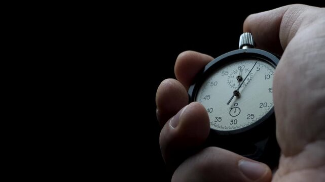 Male hand holds stopwatch and starts countdown. Second hand begins first tick. Concept of time control. Focus on precision and discipline. Dark background enhances intensity